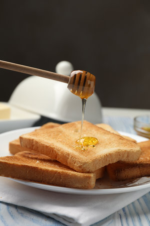 Dripping honey onto fresh toasted bread slices at light wooden table, closeupの写真素材