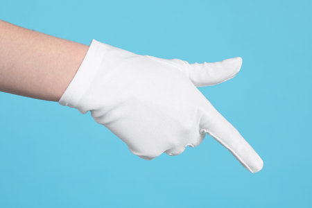Woman in cloth glove pointing at something on light blue background, closeupの写真素材