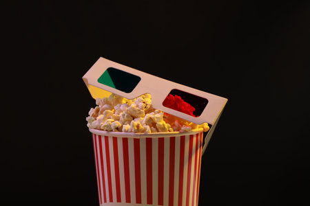 Tasty popcorn in paper cup and 3D glasses on black background, closeupの写真素材