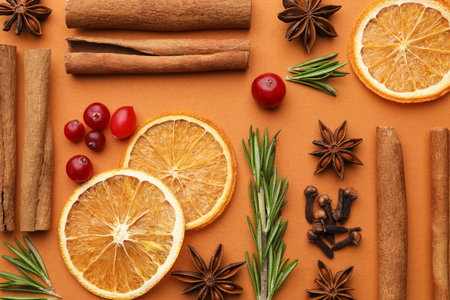 Different spices, fresh rosemary, cranberries and dry citrus slices for mulled wine on orange background, flat layの写真素材