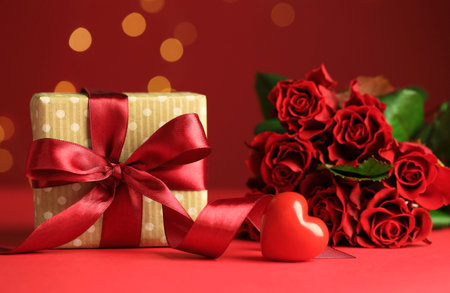 Happy Valentine's Day. Gift box, heart shaped figure and bouquet of roses on red background against blurred lights, closeupの写真素材