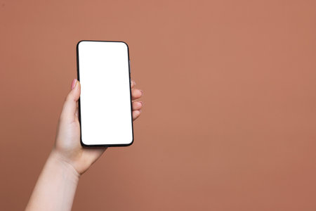 Woman holding smartphone with blank screen on brown background, closeup. Mockup for designの写真素材