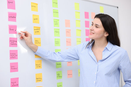 Woman giving presentation near whiteboard with sticky notes in officeの写真素材