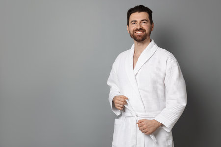 Man tying belt of bathrobe on gray background. Space for textの写真素材