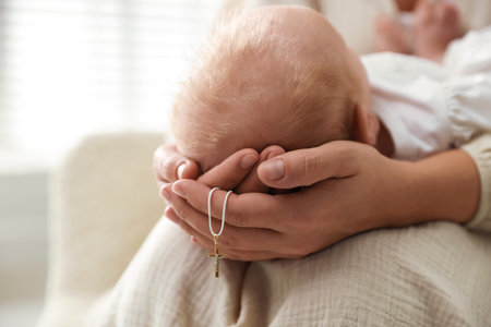 Sacrament of baptism. Woman holding little baby and gold cross indoors, closeupの写真素材
