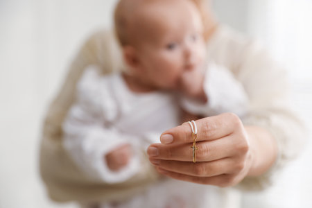 Sacrament of baptism. Woman holding little baby and gold cross indoors, selective focusの写真素材