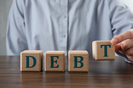 Woman making word Debt of cubes with letters on wooden table, closeupの写真素材