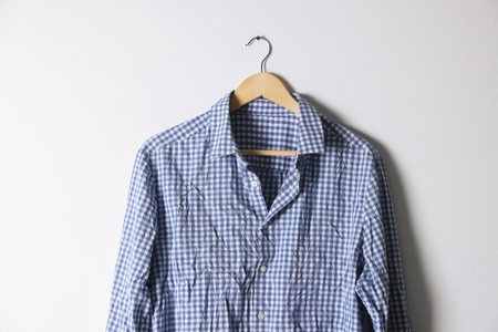 Hanger with checkered creased shirt near light wallの写真素材