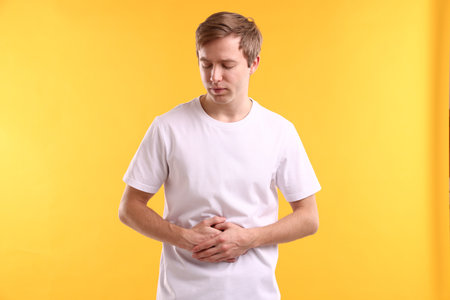 Man suffering from stomach ache on yellow backgroundの写真素材