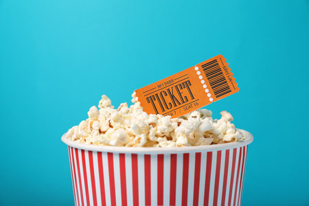 Tasty popcorn in paper cup and movie ticket on light blue background, closeupの写真素材
