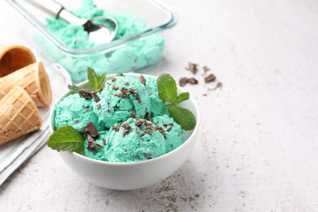 Tasty mint chocolate chip ice cream with leaves and waffle cones on light table, closeup. Space for textの写真素材