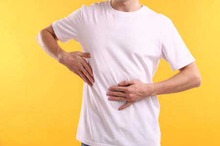 Man suffering from stomach ache on yellow background, closeupの写真素材