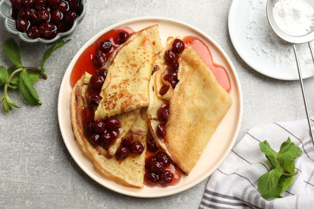 Tasty crepes with cherries, jam and mint served on light table, flat layの写真素材