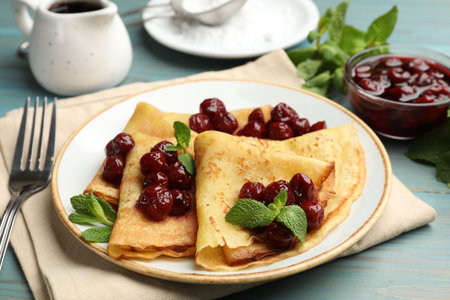 Delicious crepes served with cherry jam on light blue wooden table, closeupの写真素材