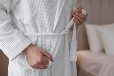 Man tying belt of bathrobe indoors, closeupの写真素材
