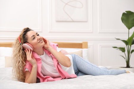 Happy woman in headphones listening music on bed near white wall at homeの写真素材