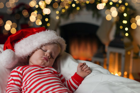 Baby in Christmas pajamas and Santa hat sleeping on bed indoors. Space for textの写真素材