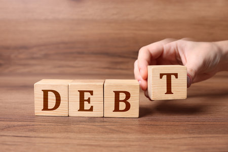 Woman making word Debt of cubes with letters on wooden table, closeupの写真素材
