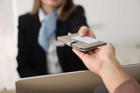 Receptionist giving passport and hotel key card to guest at reception desk indoors, closeupの写真素材