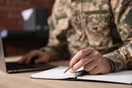 Military man working on laptop at wooden desk in office, closeupの写真素材