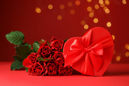 Happy Valentine's Day. Heart shaped gift box and bouquet of roses on red background against blurred lights, closeupの写真素材
