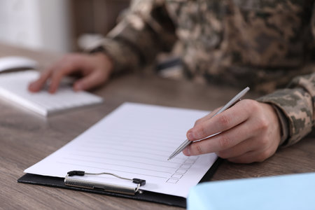 Military education. Student in soldier uniform learning at wooden desk indoors, closeupの写真素材