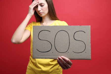 Woman holding cardboard sign with SOS on red background, closeup