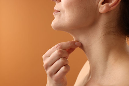 Woman touching her neck on pale orange background, closeup. Space for text