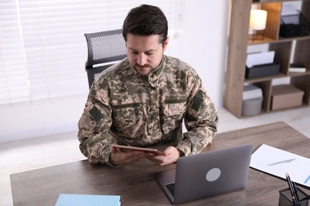 Military education. Student in soldier uniform with tablet learning at wooden desk indoors, above viewの写真素材
