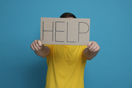 Man holding sign with word Help on light blue backgroundの写真素材