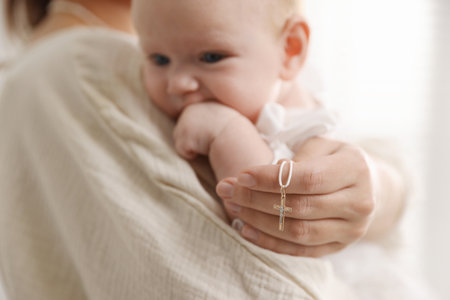 Sacrament of baptism. Woman holding little baby and gold cross indoors, selective focusの写真素材
