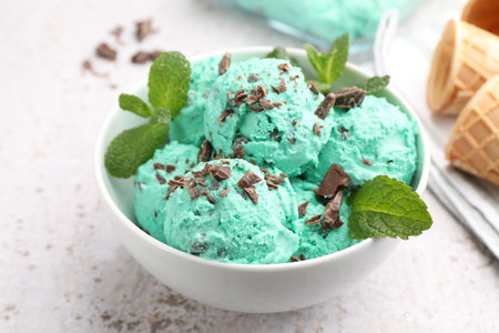Tasty mint chocolate chip ice cream with leaves and waffle cones on light table, closeup