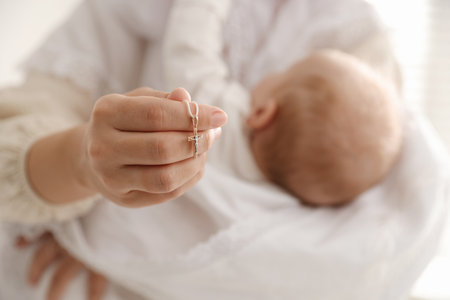 Sacrament of baptism. Woman holding little baby and gold cross indoors, selective focusの写真素材