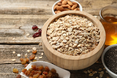 Making granola. Oat flakes in bowl, dried fruits, chia seeds, almond nuts and honey on wooden table, closeupの写真素材