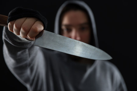 Criminal in hood with knife on black background, selective focusの写真素材