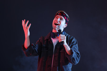 Man wearing headphones singing into microphone on dark background with smokeの写真素材