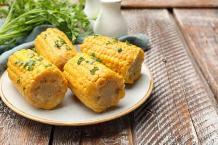 Pieces of boiled corncobs with parsley on wooden table, closeup. Space for textの写真素材