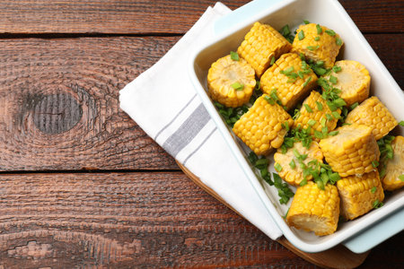 Pieces of boiled corncobs with green onion in baking dish on wooden table, top view. Space for textの写真素材
