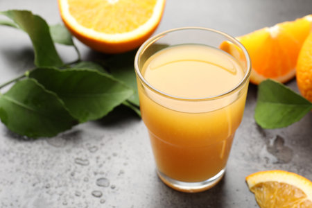 Fresh orange juice, fruits and leaves on gray table, closeupの写真素材