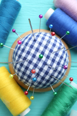 Checkered pincushion with pins, needles and spools of thread on light blue wooden background, flat layの写真素材