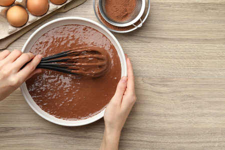 Woman mixing liquid chocolate dough at wooden table, top view. Space for text