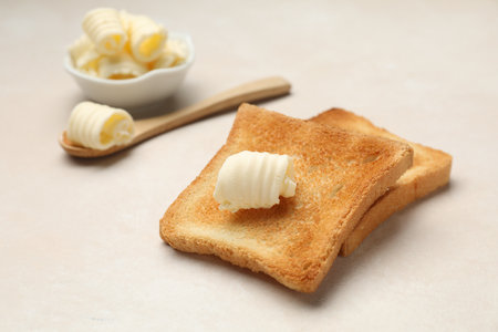 Slices of toasted bread and butter on beige table, closeupの写真素材