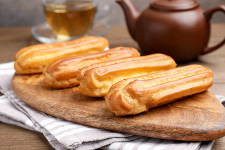 Tasty eclairs and tea on wooden table, closeup