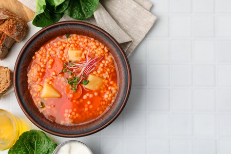Tasty lentil soup in bowl served on white tiled table, flat lay. Space for textの写真素材