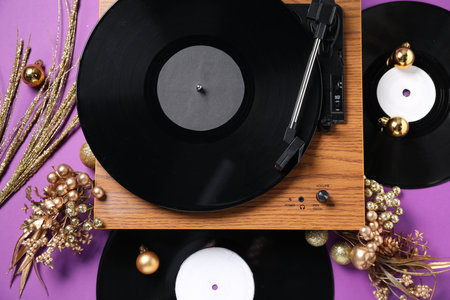Wooden turntable, vinyl records and Christmas decor on purple background, flat lay