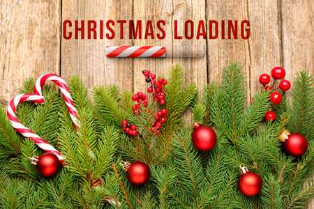 Christmas expectation. Candy cane as loading bar. Fir tree branches with red festive balls on wooden background, flat layの写真素材