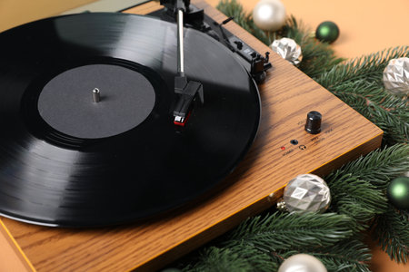 Wooden turntable with vinyl record and Christmas decor on beige background, closeup