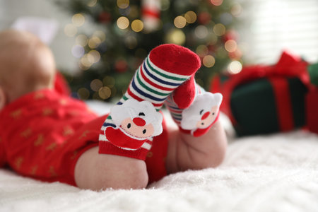 Baby in Christmas socks on bed against blurred lights indoors, closeupの写真素材