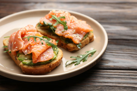 Tasty bruschetta with salmon, avocado, arugula and sesame seeds on wooden table, closeupの写真素材