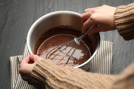 Woman mixing liquid chocolate dough at black table, closeup